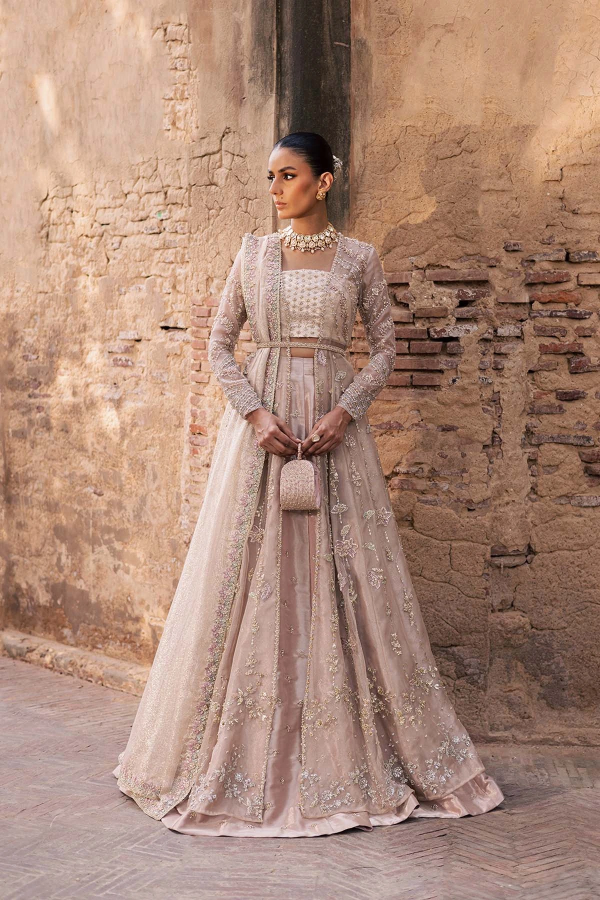 Dusty-rose and champagne formal lehenga with a long embroidered jacket against a tan brick wall